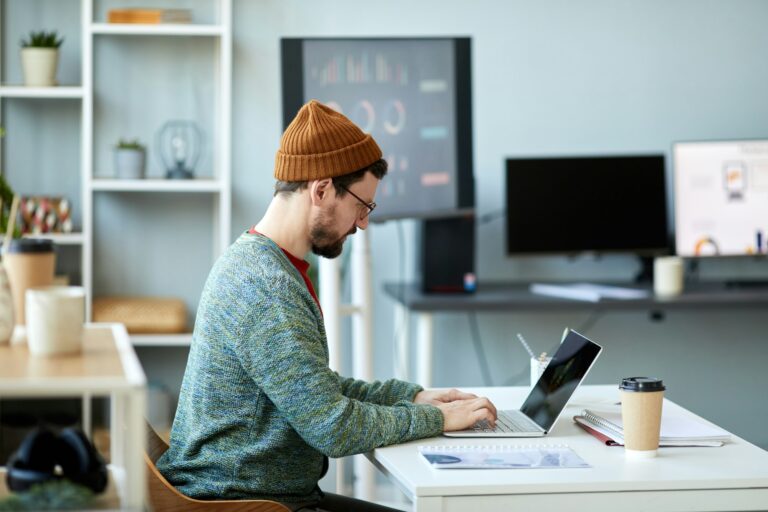 Young male employee or designer sitting in front of laptop and networking